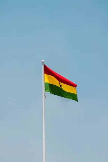 La bandiera nazionale del Ghana sventola su un'asta bianca contro un cielo azzurro limpido.