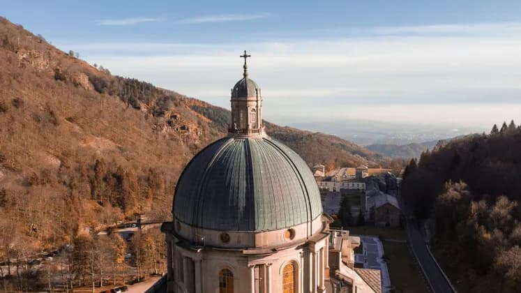 La cupola verde di un grande santuario, sormontata da una croce, è vista dall'alto su uno sfondo di montagne autunnali.