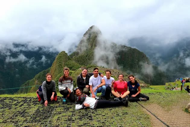 Un viaje en grupo de WeRoad posa para una foto en un mirador cubierto de hierba, con montañas cubiertas de niebla al fondo.