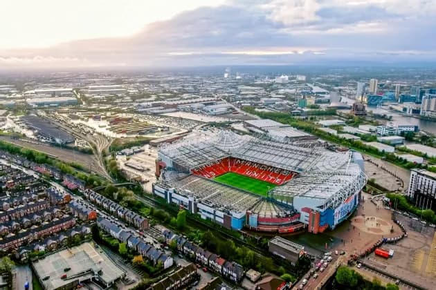 Una veduta aerea di un grande stadio di calcio circondato da case residenziali, ferrovie e un ampio paesaggio urbano.