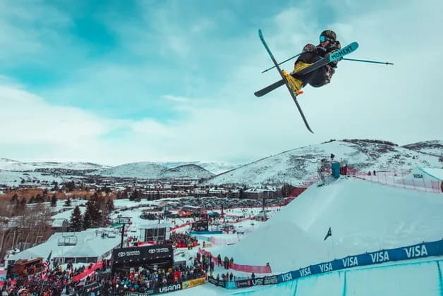 Un sciatore esegue una presa acrobatica aerea a mezz'aria sopra una rampa di neve in una competizione di sport invernali.