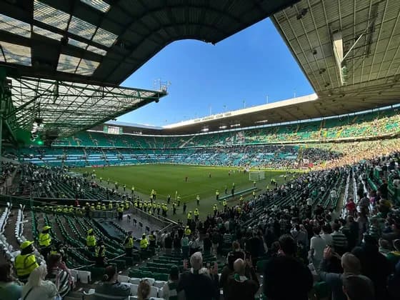 La folla riempie gli spalti verdi dello stadio di fronte a un campo da soleggiato sotto un cielo blu limpido