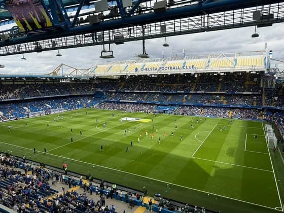 I giocatori si riscaldano su un campo verde brillante all'interno di uno stadio di calcio gremito prima di una partita.
