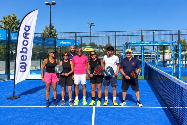 Un gruppo di persone con le racchette in posa su un campo da padel all'aperto sotto un cielo limpido e luminoso.