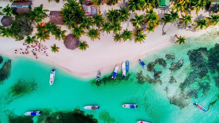 Une vue aérienne d'un voyage en groupe WeRoad sur une plage de sable blanc bordée de palmiers, à côté de bateaux dans des eaux turquoise.