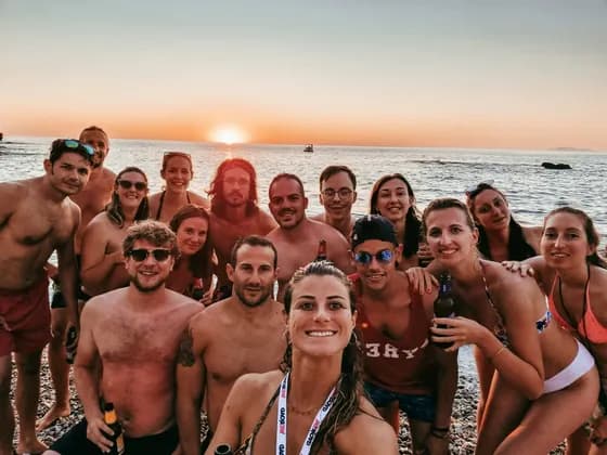 Un viaggio di gruppo WeRoad scatta un selfie su una spiaggia di ciottoli al tramonto sul mare.