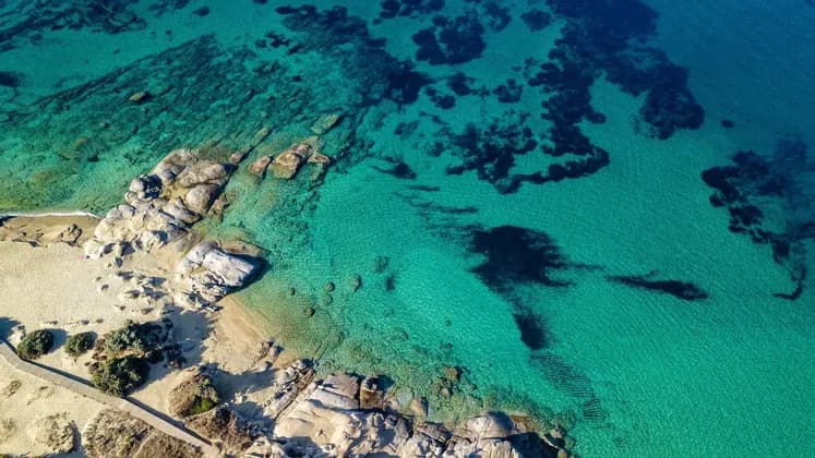 Una vista aerea di una costa rocciosa con una spiaggia sabbiosa, delimitata da acque marine limpide e turchesi.