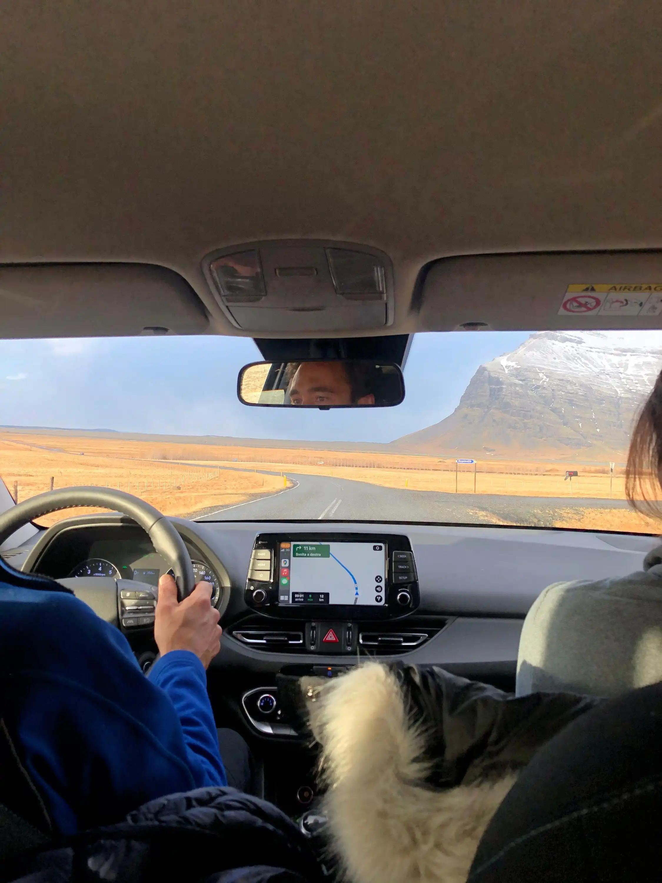 View from inside a car as a WeRoad group trip drives along a road towards a snow-capped mountain with GPS navigation active.