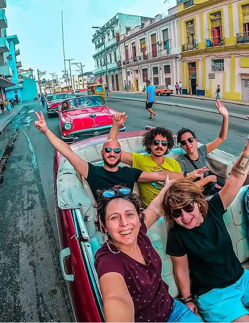 Un grupo de WeRoad se toma una selfie mientras pasea en un descapotable rojo clásico por una calle de la ciudad.