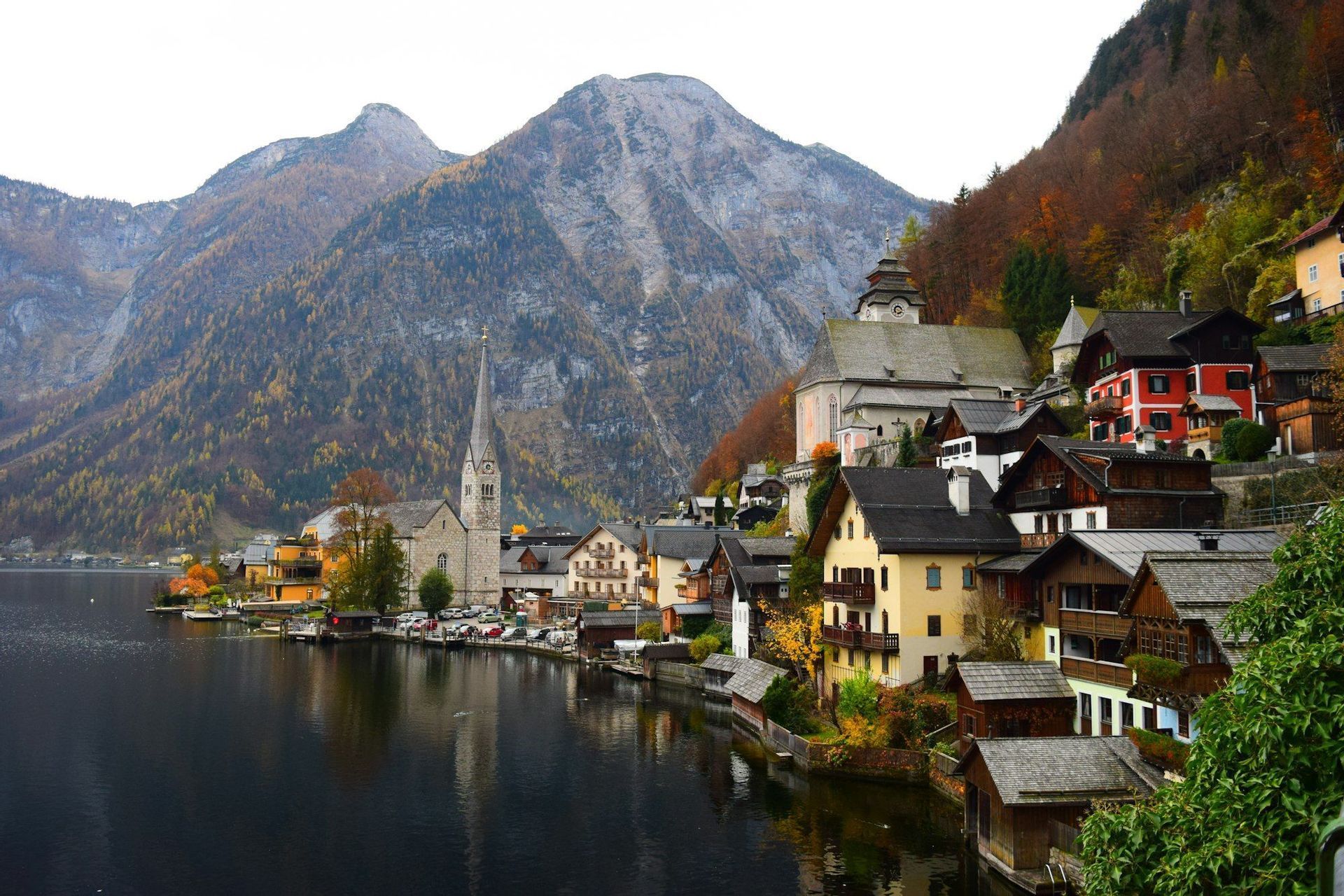 Un village lacustre avec un clocher d'église imposant est situé au pied de grandes montagnes en automne.