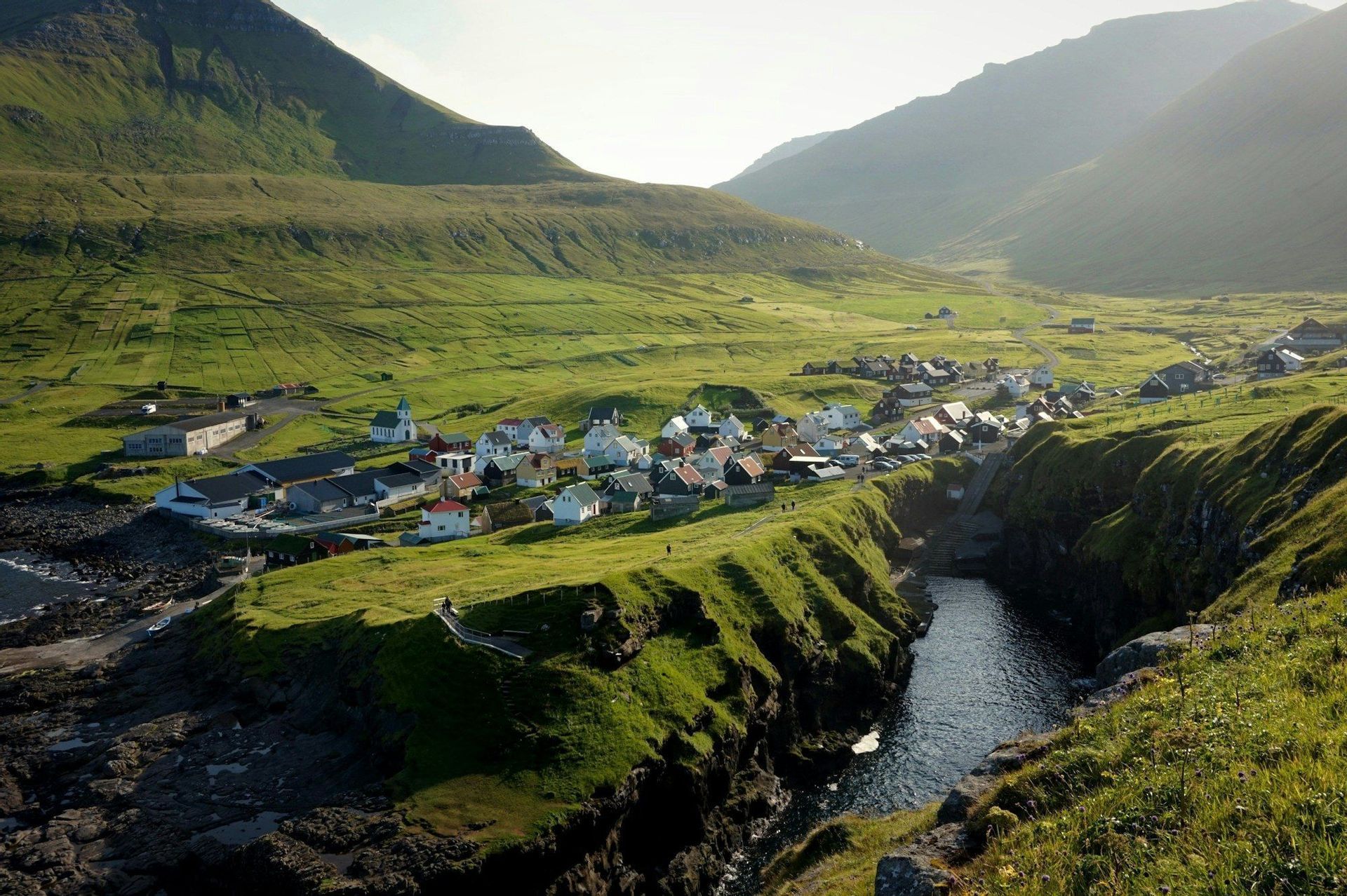 Un village côtier coloré niché dans une vallée verdoyante luxuriante, perché sur une falaise au-dessus d'une étroite crique marine et entouré de collines.