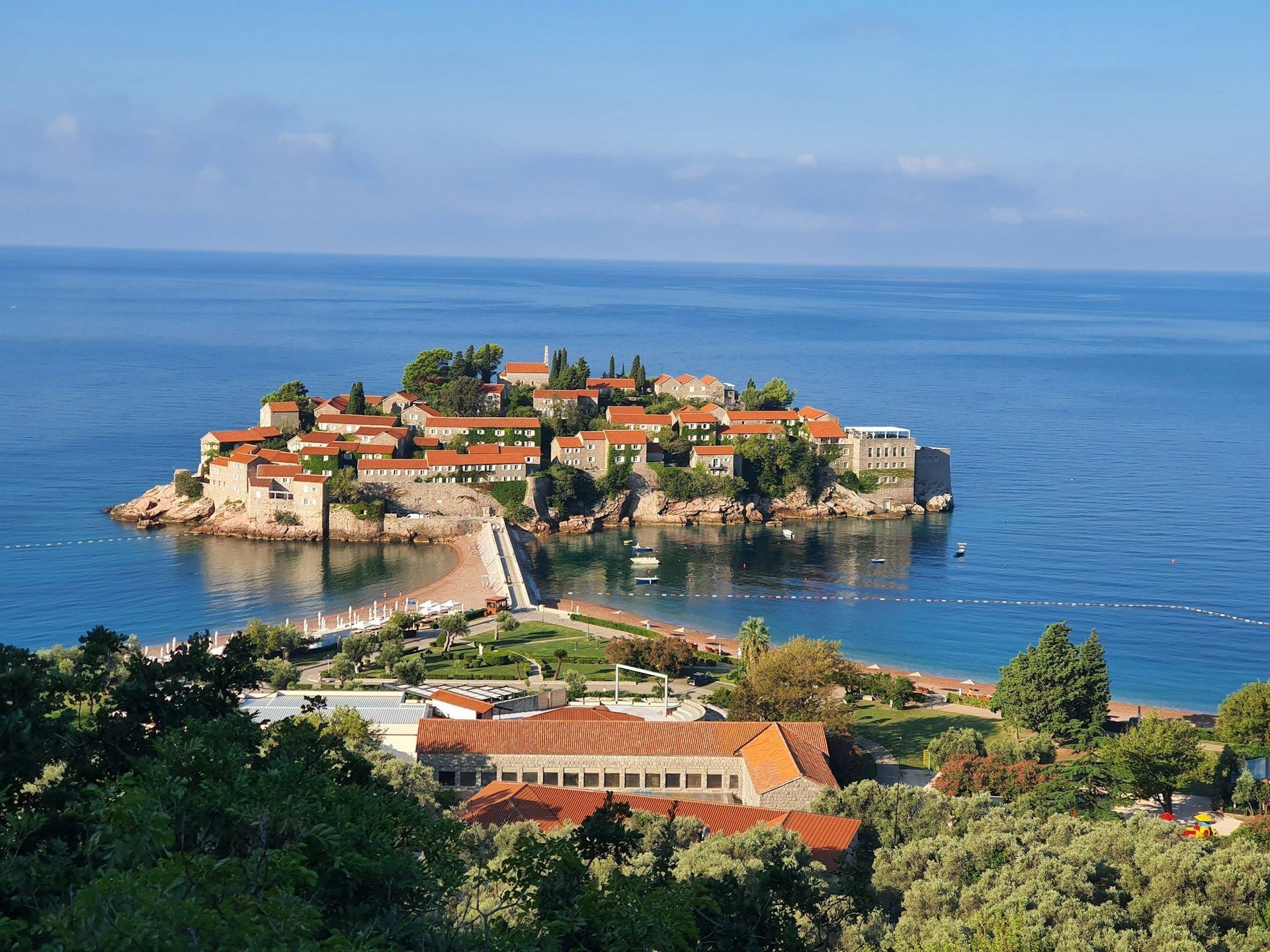 Una vista dall'alto di una piccola isola fortificata con edifici dai tetti rossi, collegata da una stretta strada rialzata a una spiaggia.