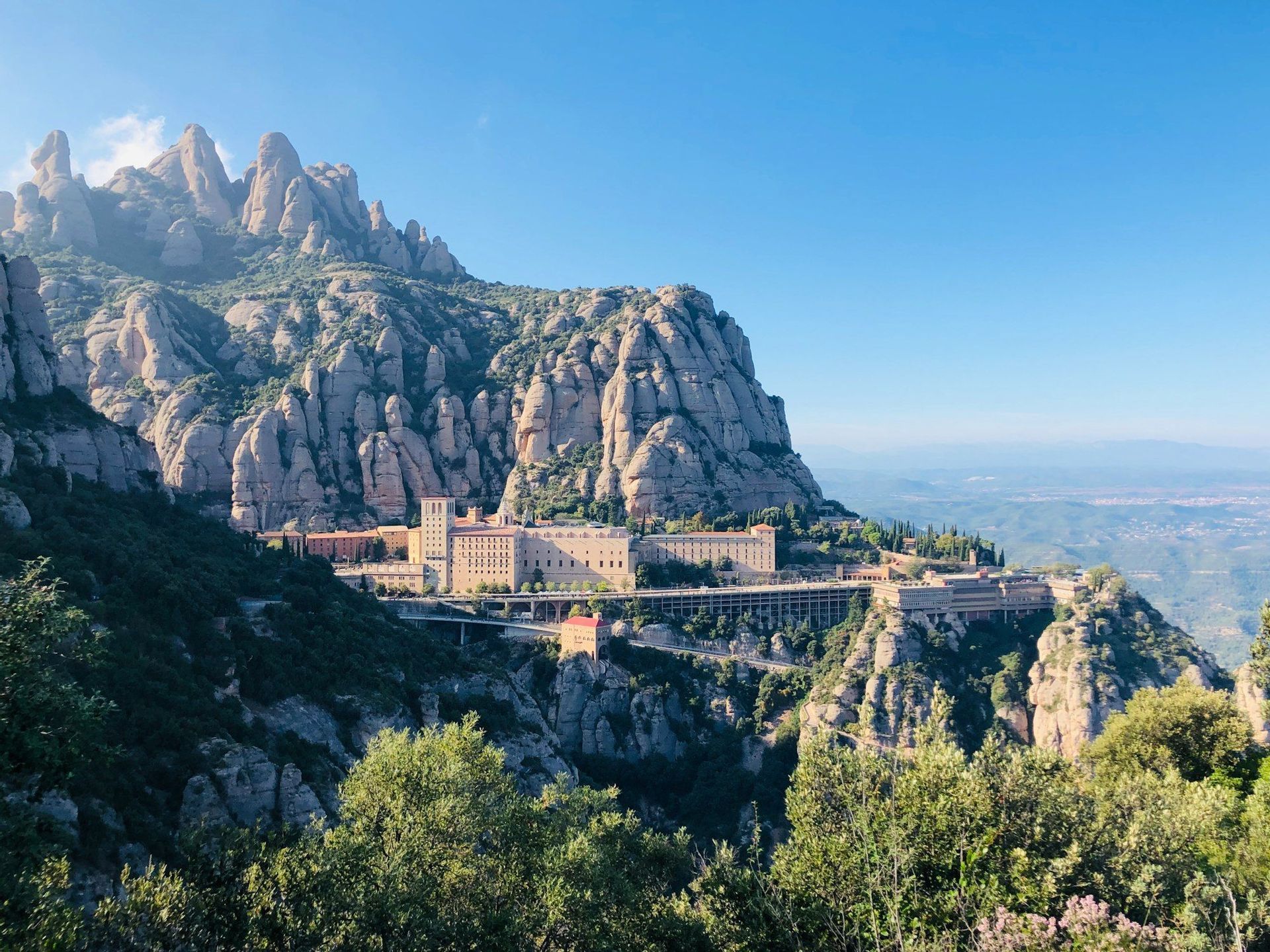 Un gran complejo monástico construido en la ladera de una montaña rocosa escarpada y con múltiples picos bajo un cielo azul claro.