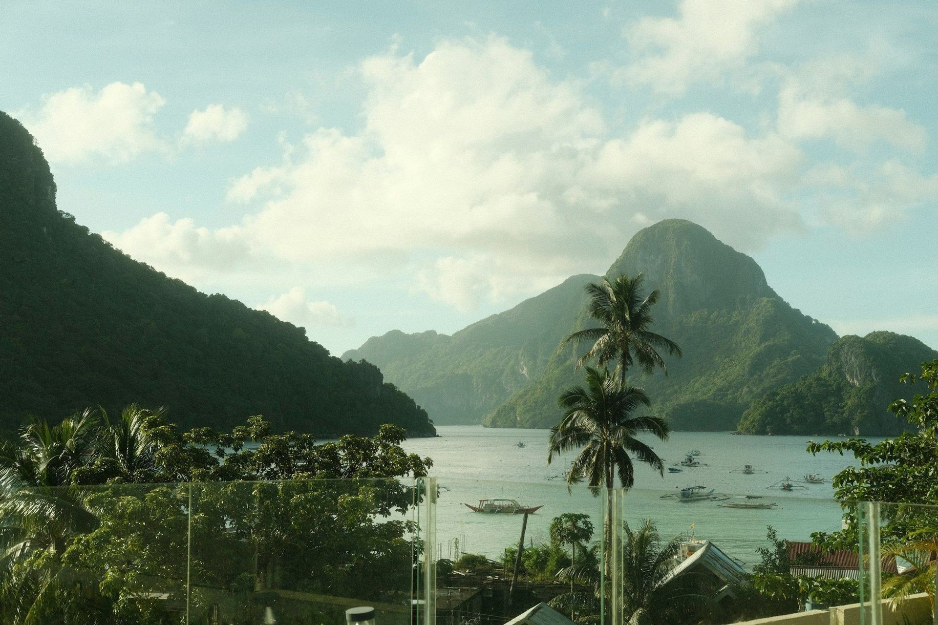 Una vista panorámica de una bahía tropical con barcos, rodeada de exuberantes montañas verdes bajo un cielo parcialmente nublado.