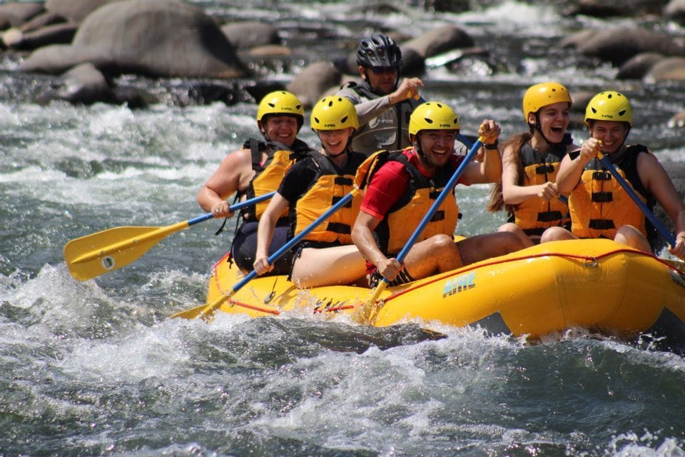 Eine WeRoad-Gruppenreise von Personen mit gelben Helmen, die lachend in einem Schlauchboot auf einem reißenden Fluss Wildwasser-Rafting machen.