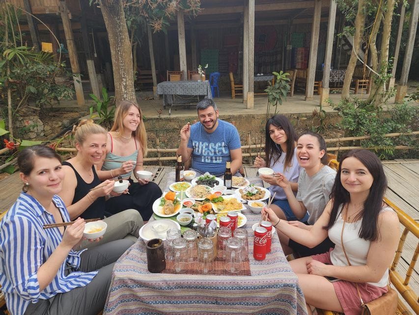 A WeRoad group trip sits at a large outdoor table, smiling and sharing a meal with many different dishes.