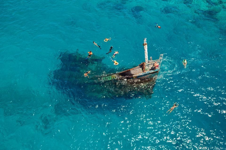 Eine Luftaufnahme einer WeRoad Gruppenreise, die um ein Schiffswrack in leuchtend türkisfarbenem Wasser schnorchelt.