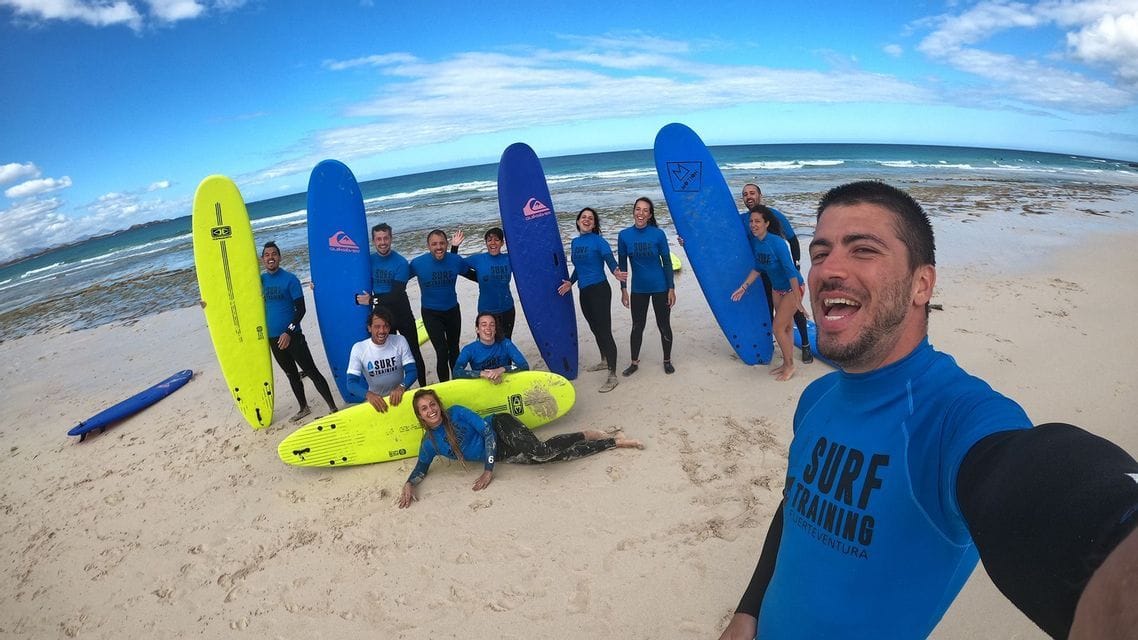 Un grupo de WeRoad, con camisetas azules a juego, se toma una selfie en una playa mientras sostienen sus tablas de surf.