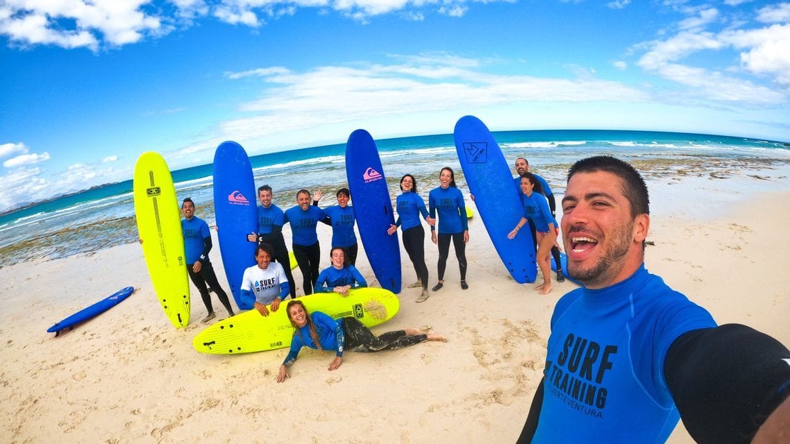 Un groupe WeRoad en t-shirts de surf assortis pose pour un selfie avec des planches de surf sur une plage de sable.