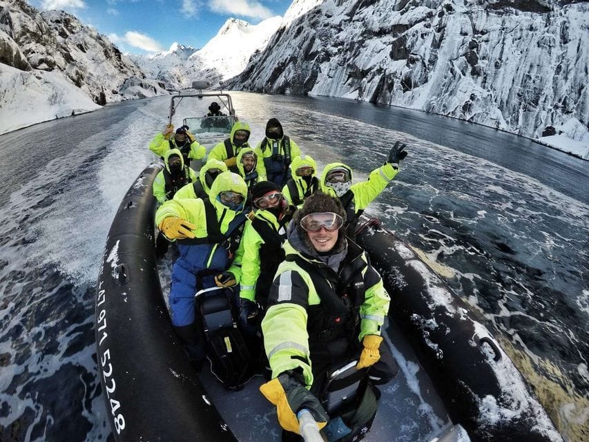 A WeRoad group trip in bright winter gear takes a selfie on a boat navigating a fjord between snowy mountains.