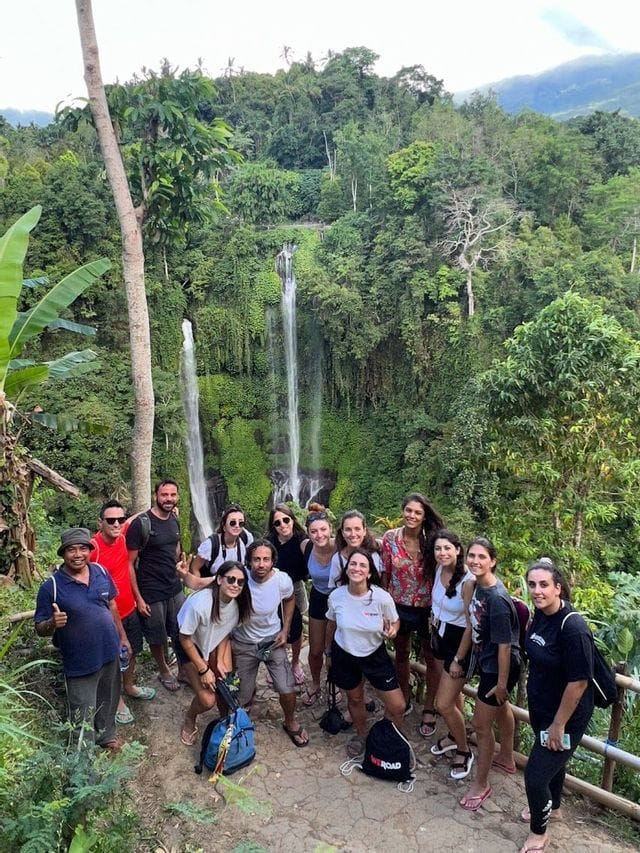 Un grupo de WeRoad posa para una foto en un sendero selvático, con una cascada alta y escalonada visible al fondo.