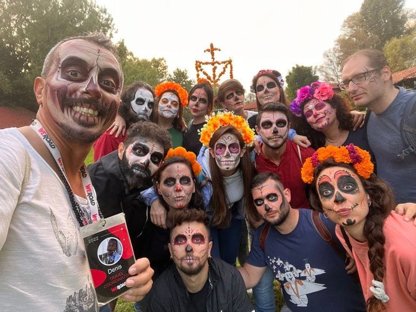 Eine WeRoad-Gruppe posiert für ein Selfie mit als Calavera-Totenschädel bemalten Gesichtern, einige tragen Blumenkränze.