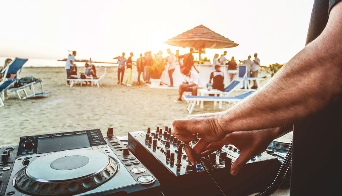 Un DJ che mixa musica per una festa di gruppo WeRoad in spiaggia al tramonto.