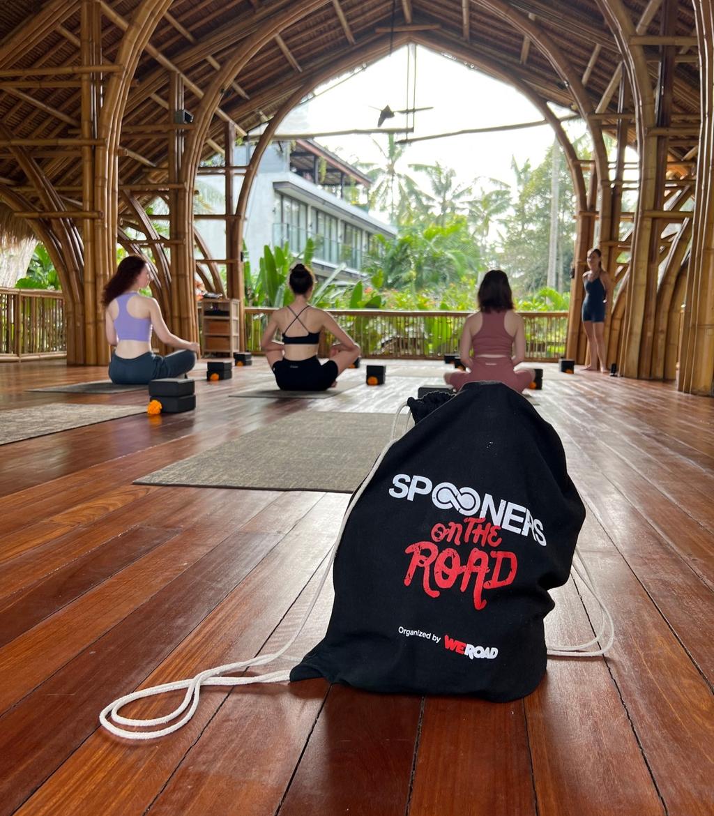 A WeRoad drawstring bag on the floor of a bamboo pavilion in Bali, Spooners doing yoga behind it