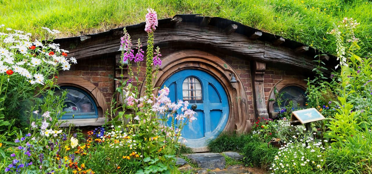 Una casa in stile hobbit, con una porta blu rotonda, incastonata in una collina erbosa e circondata da un lussureggiante giardino di fiori colorati.