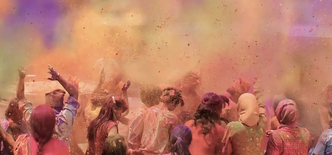 Un voyage de groupe WeRoad fait la fête au milieu d'une foule, jetant des nuages de poudre colorée en l'air lors d'un festival.