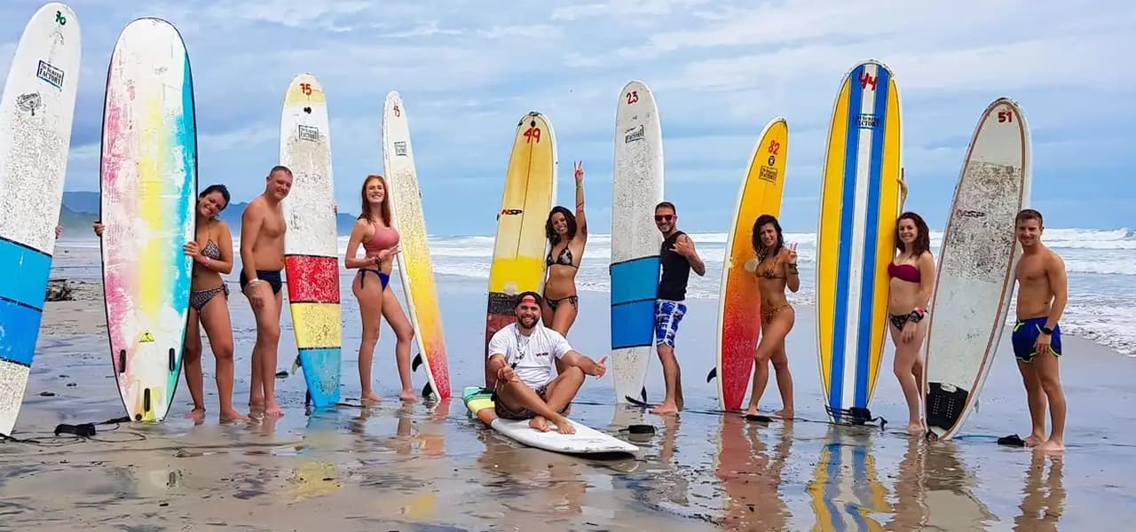 Un viaggio di gruppo WeRoad in posa con tavole da surf colorate su una spiaggia sabbiosa e bagnata, in riva all'oceano.
