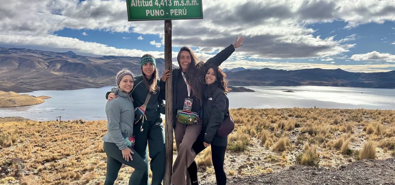 Quatre voyageuses WeRoad qui prennent la pose devant un panneau d'altitude, avec un lac de montagne en toile de fond.