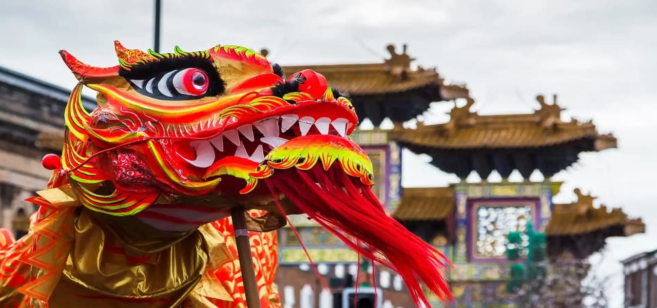 Gros plan d'une tête de dragon chinois rouge et or, très colorée, lors d'un festival en plein air, avec une arche traditionnelle en arrière-plan.