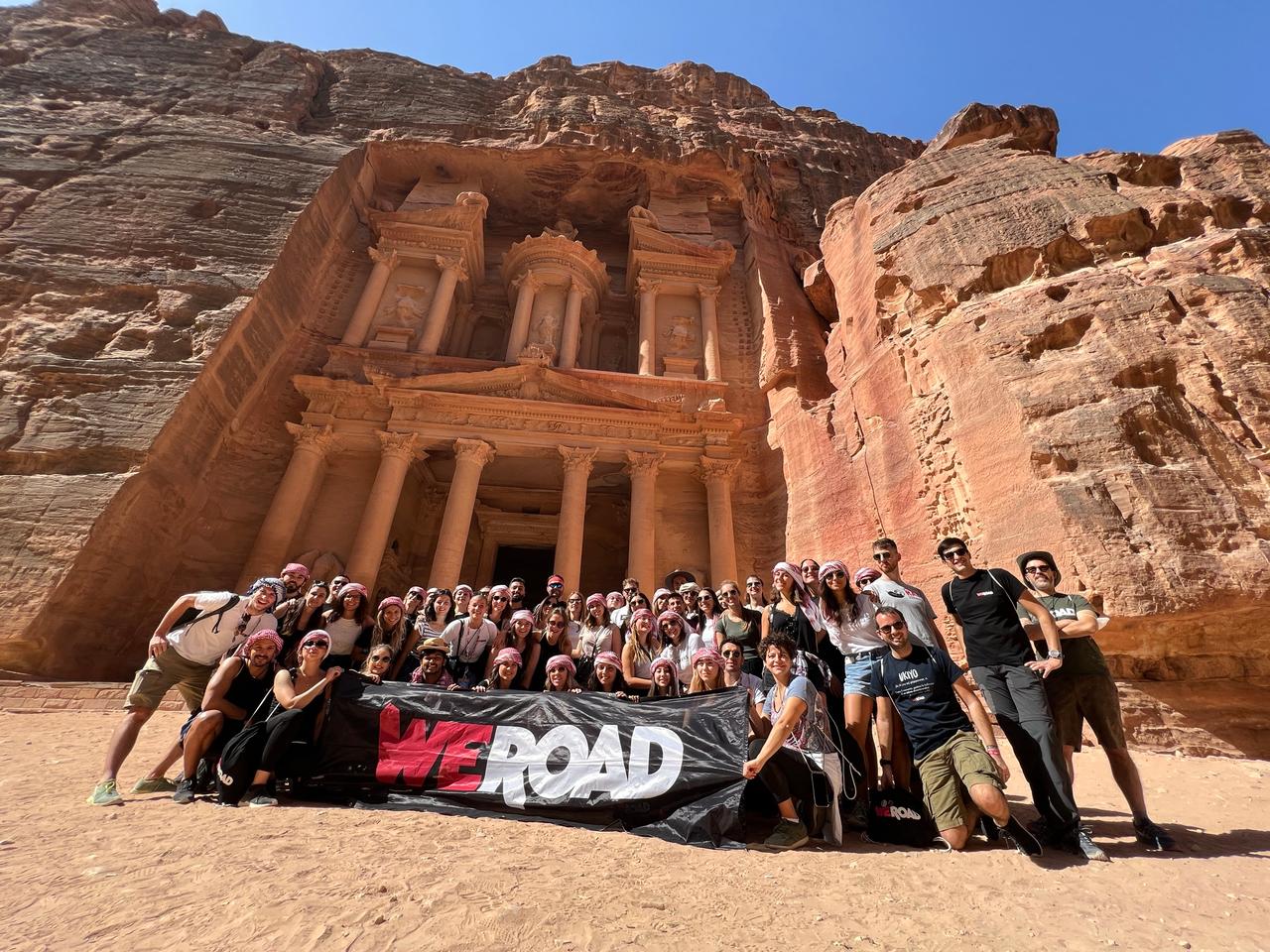 A large WeRoad group trip holding the WeRoad banner in front of the Treasury in Petra