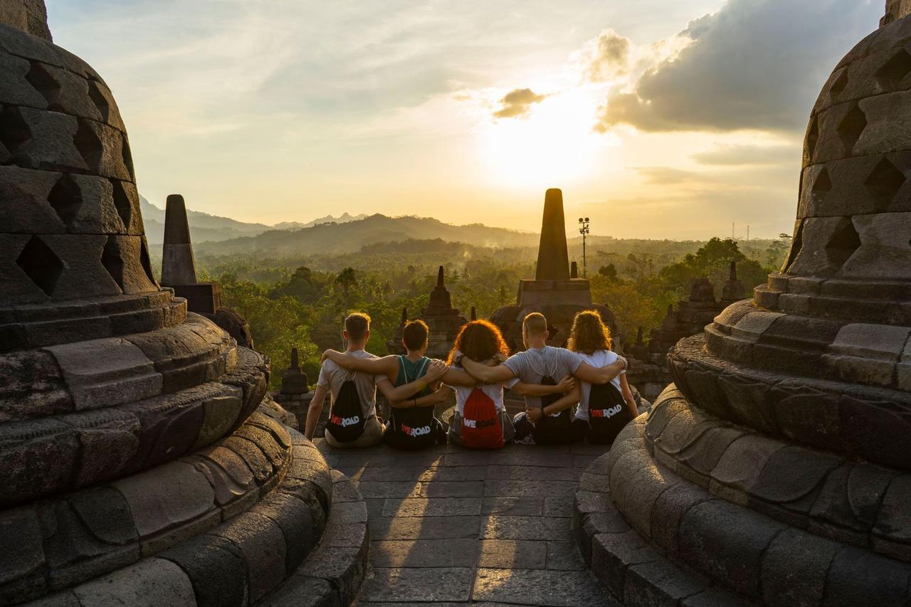 Un grupo de WeRoad se sienta con los brazos entrelazados en un templo de piedra, observando el amanecer sobre un paisaje exuberante y montañoso.