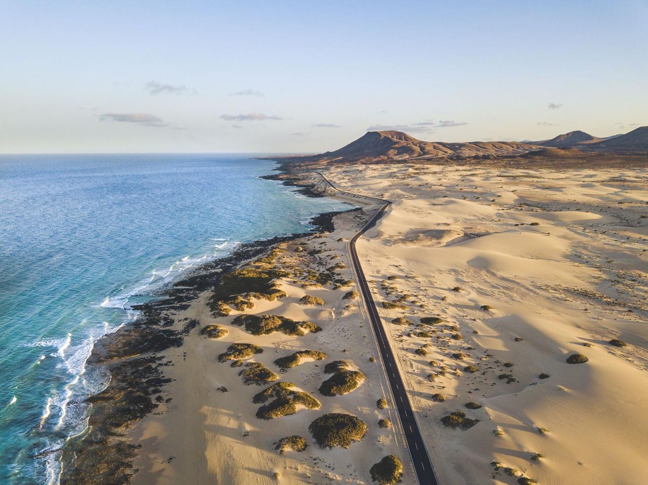 Vista aerea di una strada asfaltata che si snoda lungo la costa, separando vaste dune di sabbia dall'oceano blu.