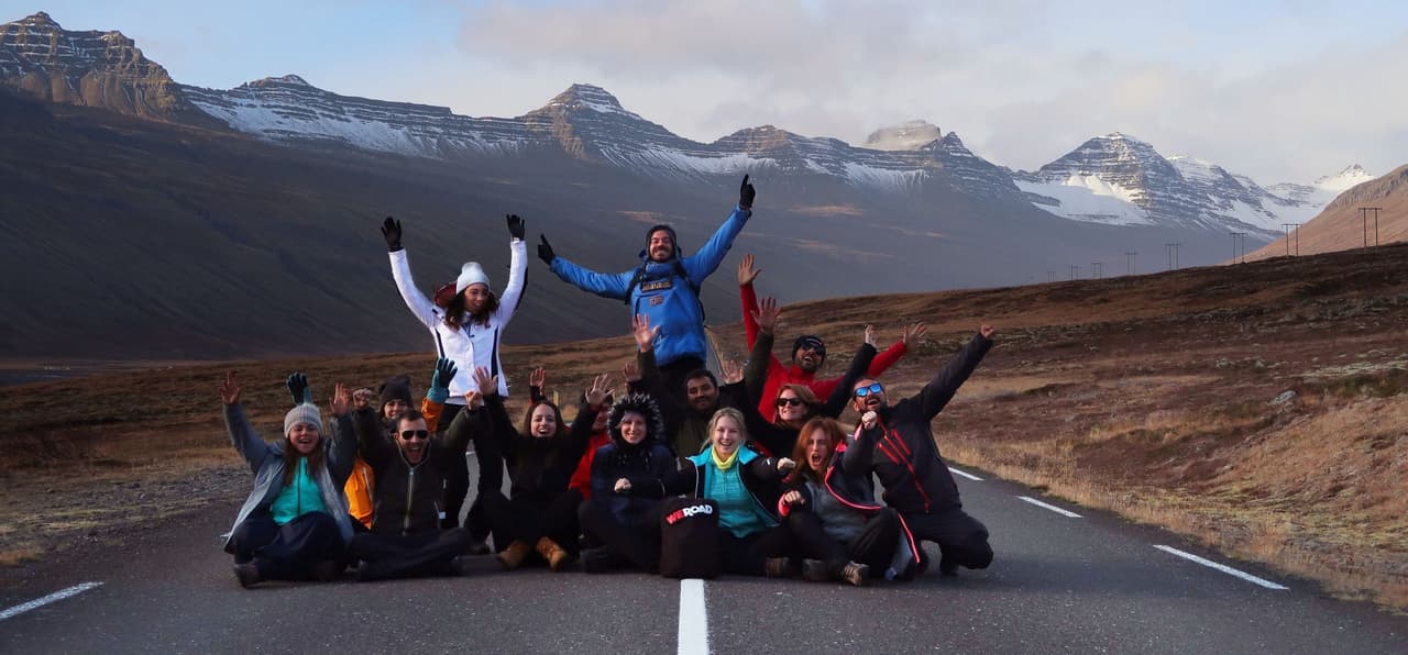 Un gruppo WeRoad posa per una foto, seduti e in piedi su una strada con uno sfondo di montagne innevate.