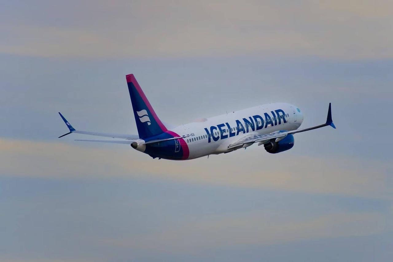 Un avión de Icelandair volando a través de un cielo parcialmente nublado, visto de lado.