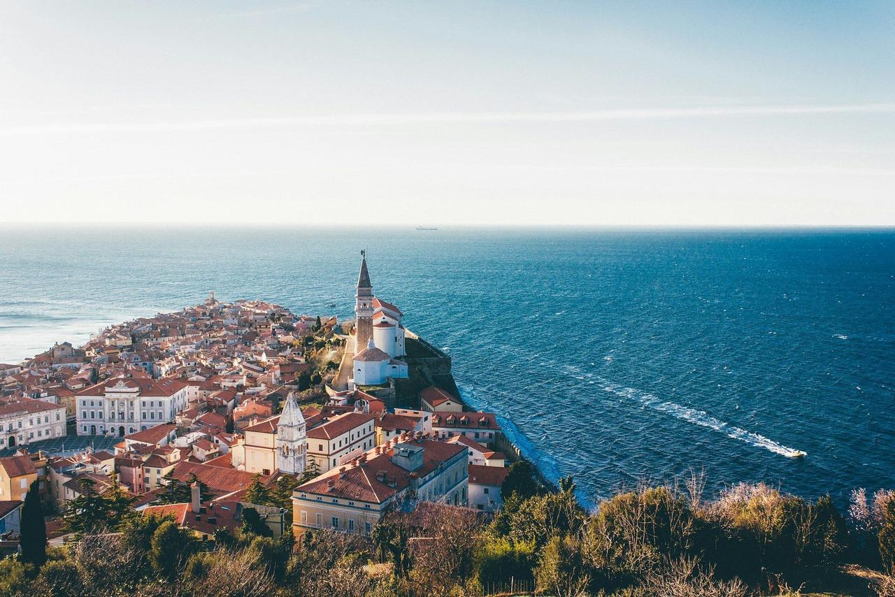 Une vue aérienne d'une ville côtière sur une presqu'île, avec des bâtiments aux toits rouges et une église dominant la vaste mer bleue.