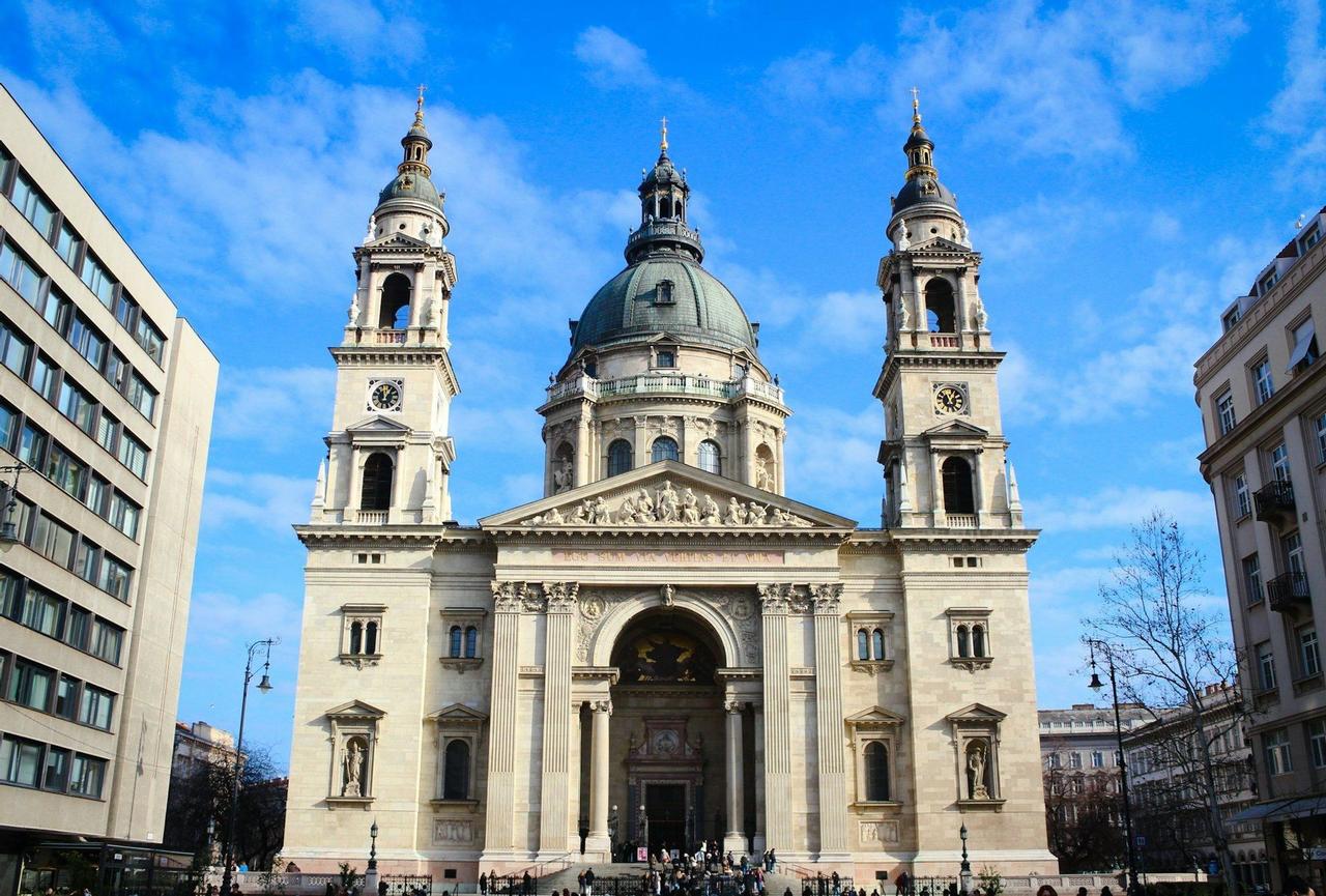La gran fachada de una basílica neoclásica con una gran cúpula central y dos campanarios bajo un cielo azul brillante.