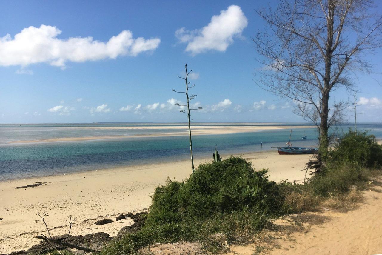 Un bateau repose sur une plage de sable près d'une eau turquoise peu profonde avec des bancs de sable sous un ciel bleu.