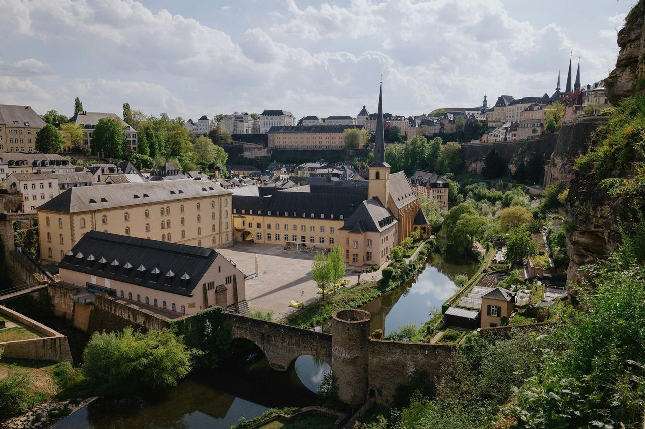 Vue en hauteur d'une ville européenne historique avec une église, des bâtiments en pierre et un pont en arc enjambant une rivière sous un ciel nuageux.
