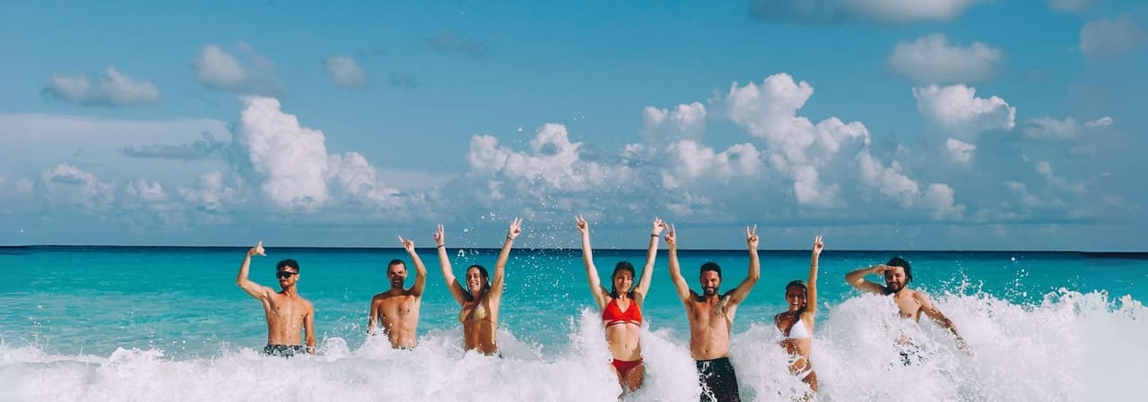 Un groupe WeRoad se tient dans les vagues turquoise de l'océan, souriant, les bras levés, faisant des signes de paix.