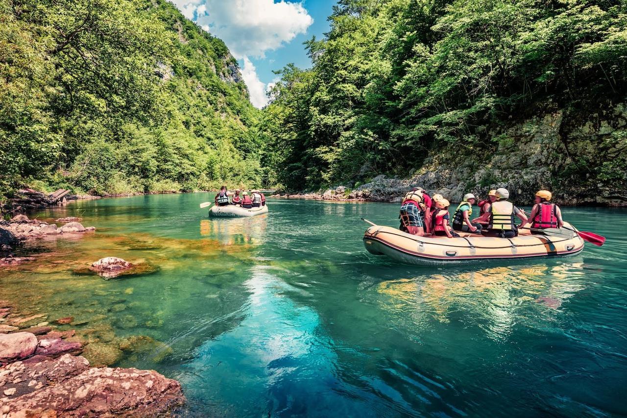 Un viaje en grupo de WeRoad para hacer rafting en dos balsas inflables en un río turquesa que serpentea por un exuberante cañón verde.