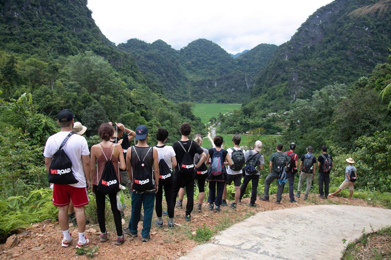 Un voyage en groupe WeRoad vu de dos, contemplant une vaste vallée verte entourée de montagnes.