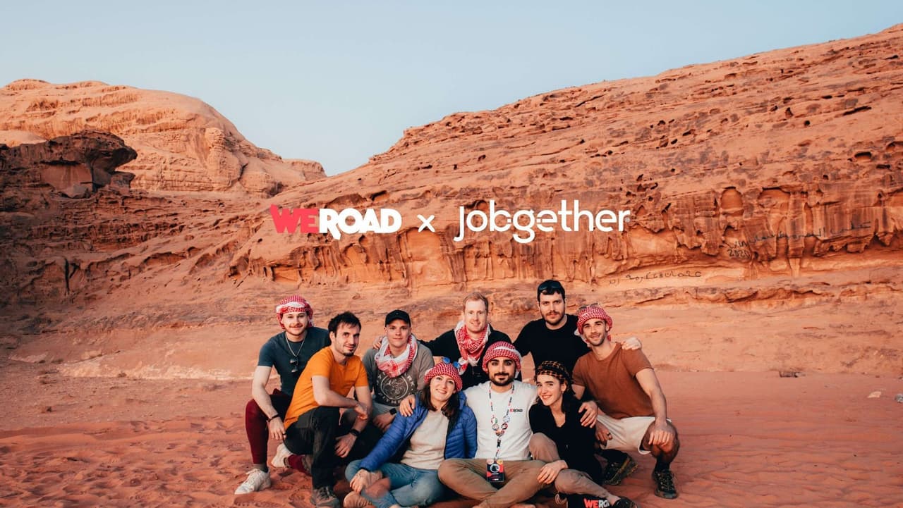 A WeRoad group trip of nine people posing for a photo in a desert landscape with red rock formations in the background.