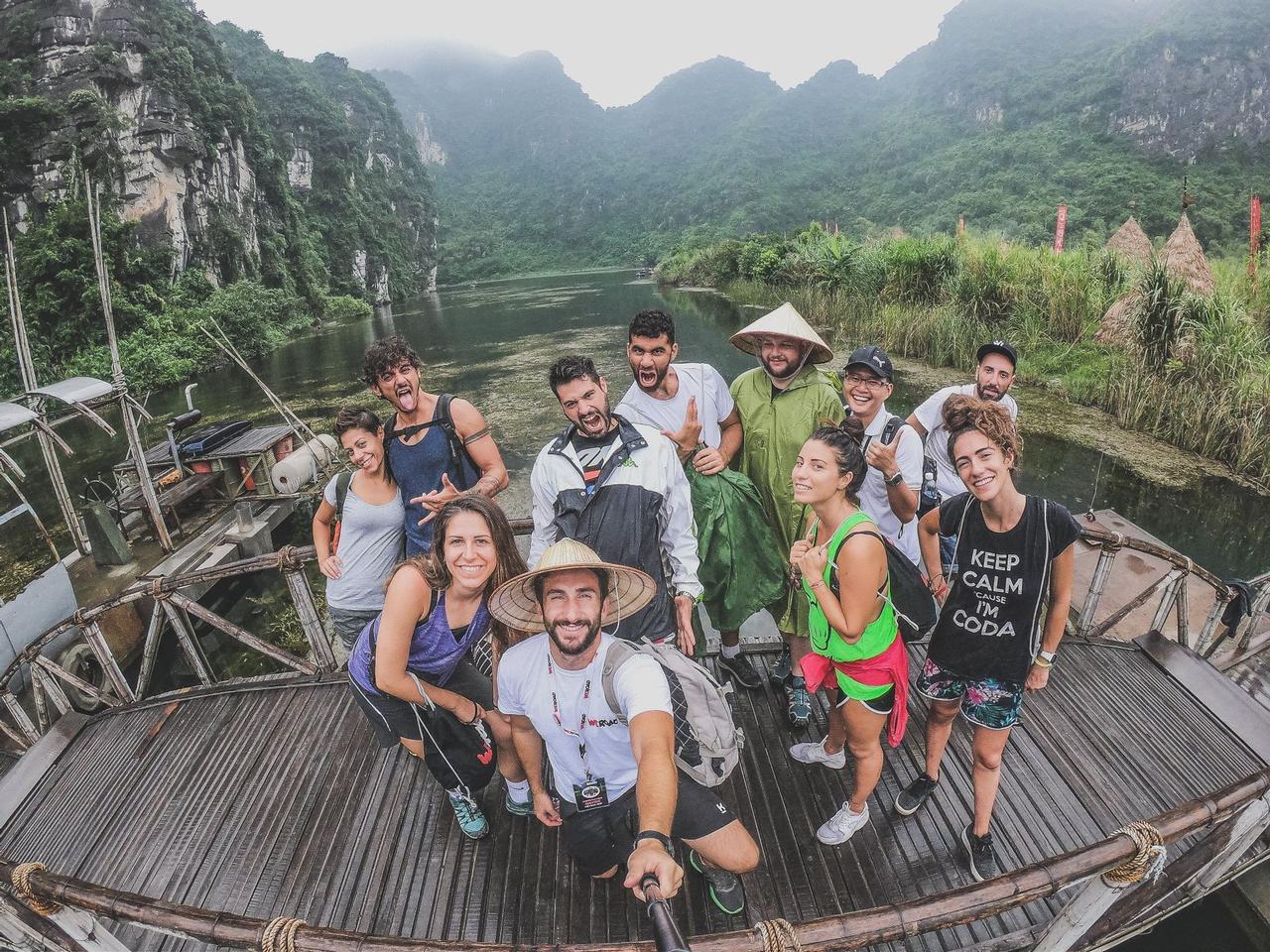 Un grupo de WeRoad saca una selfie en un barco de madera con un río y montañas verdes de fondo.