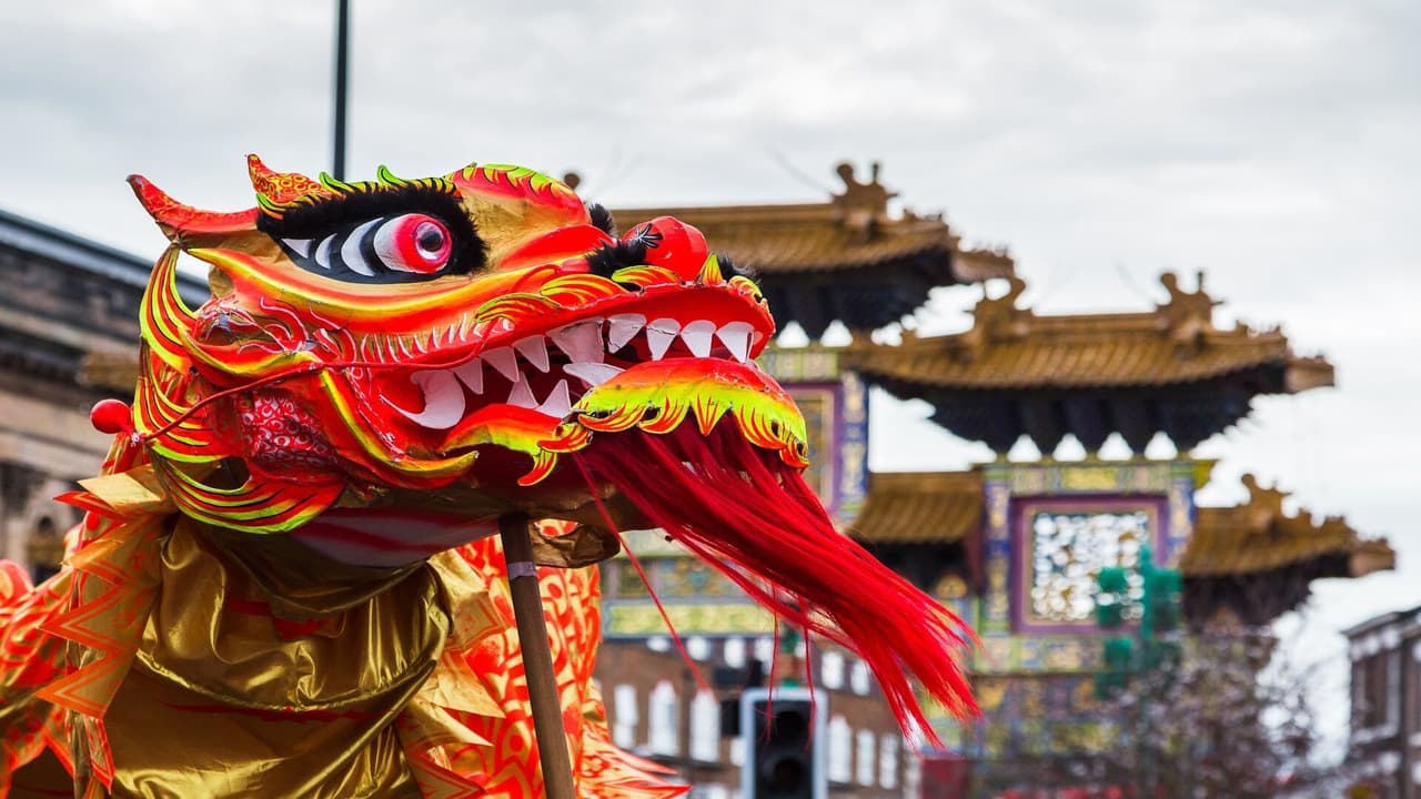 Primo piano di una testa di marionetta di drago cinese, rossa e oro, vivacemente colorata, a un festival all'aperto, con un arco tradizionale sullo sfondo.