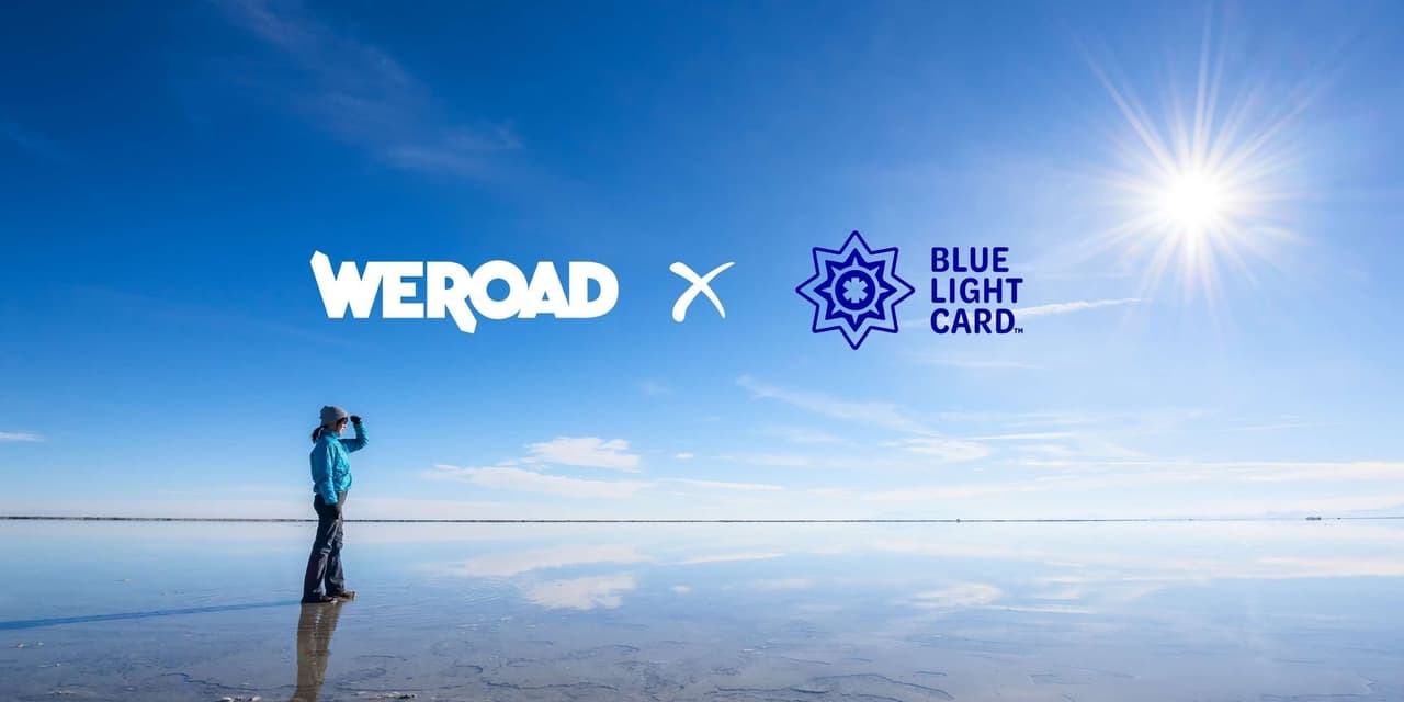A person stands on a reflective water surface, gazing at the horizon under a blue sky with WeRoad and Blue Light Card logos.