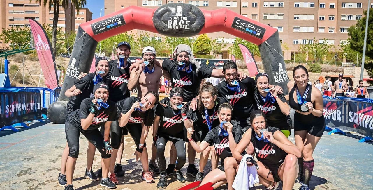 Un grupo de viaje de WeRoad posa para una foto, mordiendo sus medallas debajo de un arco inflable de 'Survivor Race' después de completar el evento.